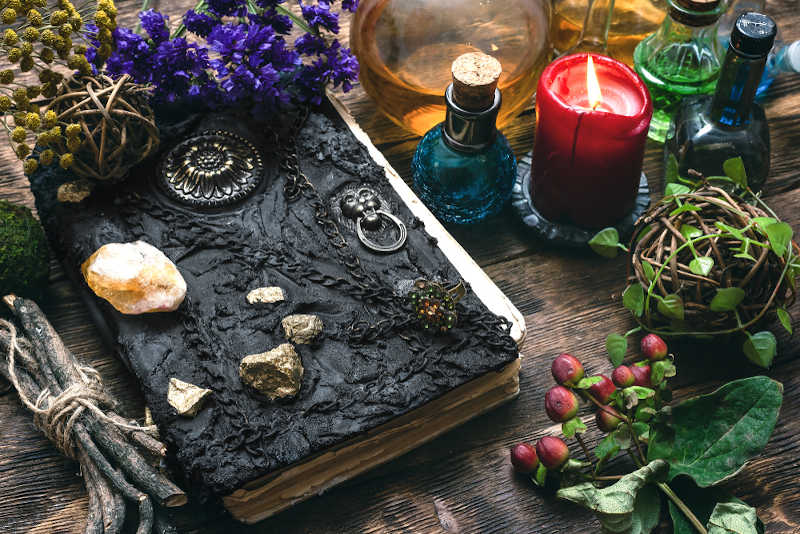 A book of shadows used in Alexandrian Wicca surrounded by crystals, herbs and candles.