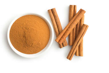 Freshly grounded cinnamon in a bowl next to cinnamon sticks. 