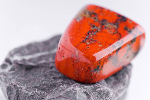 A red jasper gemstone with magical and metaphysical properties sitting on a rock surface. 