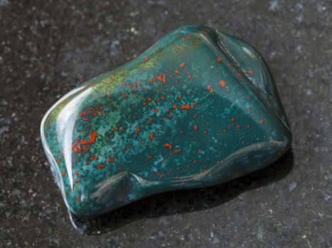 A bloodstone gemstone with magical and metaphysical properties on black marble. 